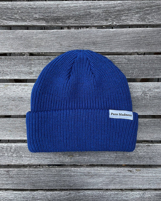 Blue Captain Merino Beanie – koboltblå merinoull-lue med Pure Madness-merke på grå treplanker