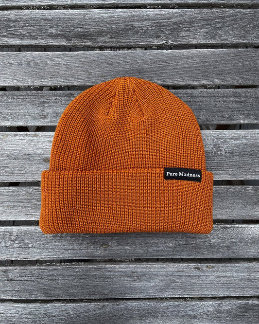 Orange Captain Merino Beanie – oransje merinoull-lue med Pure Madness-merke på grå treplanker