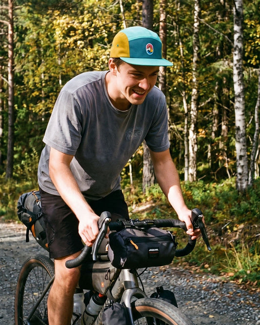 5 Panel Cap Forest Sunrise – mann på sykkeltur med bikepacking på grusvei i skogen
