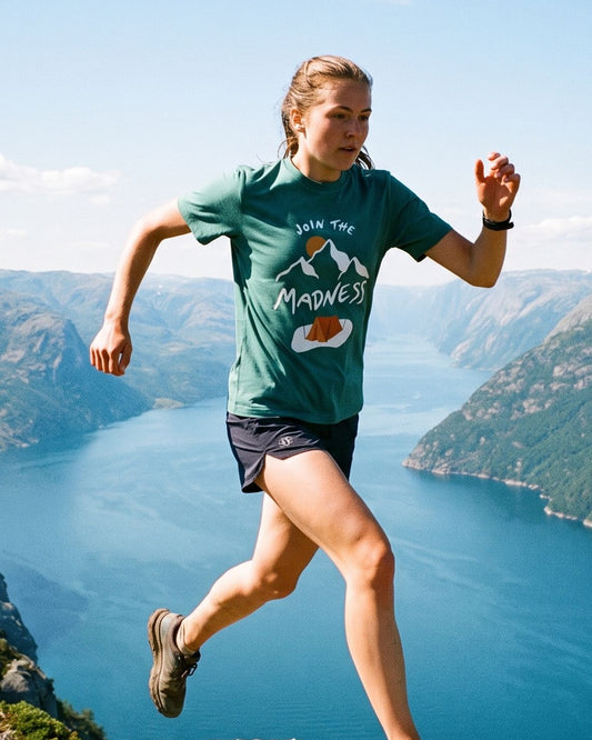 Join the Madness Teal Tee – kvinne i fjelløp langs en egg over fjorden