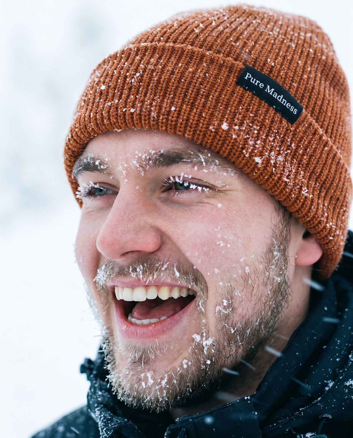 Orange Captain Merino Beanie – nærbilde av leende mann med snø i skjegget i snøstorm