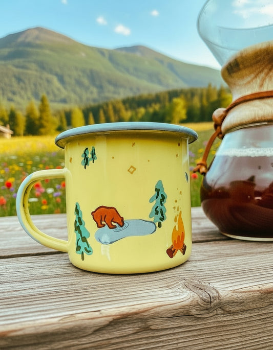 Brother Bear Enamel Mug – kruset med bjørn, trær og bål på et trebord ved kaffekanne
