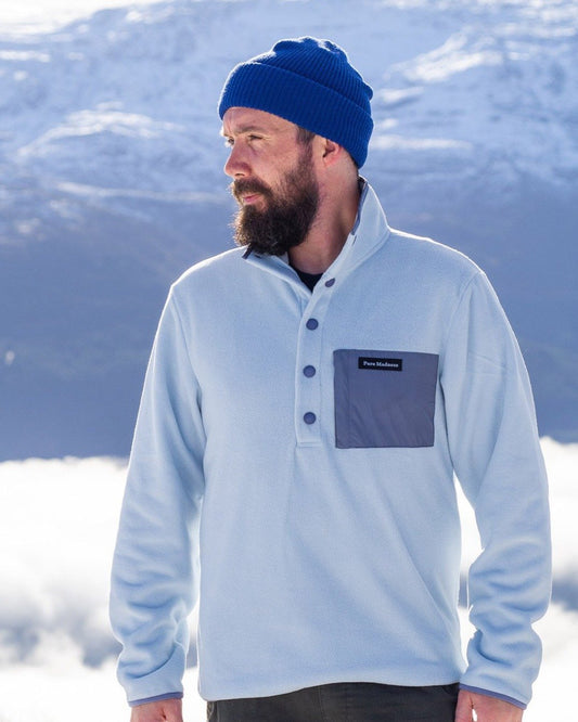 Fresh Powder Fleece – mann med skjegg i lyseblå fleece med brystlomme foran snødekte fjell