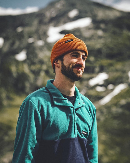 Polar Fleece – smilende mann med oransje lue i fleecen foran fjell