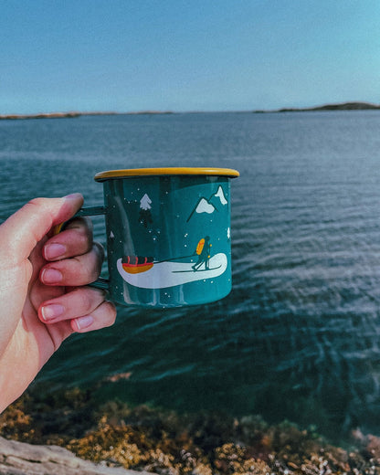 Winter Explorer Enamel Mug – hånd holder kruset med skiløpermotiv over sjøen