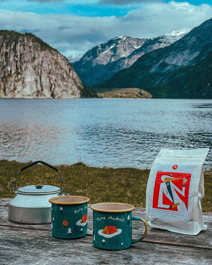 Winter Explorer Enamel Mug – to krus, kjele og kaffepose på et bord ved en fjord